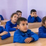 تلاميذ بالزي الأزرق الموحد يجلسون على المقاعد الخشبية مع انطلاق عودة الطلاب إلى المدارس.